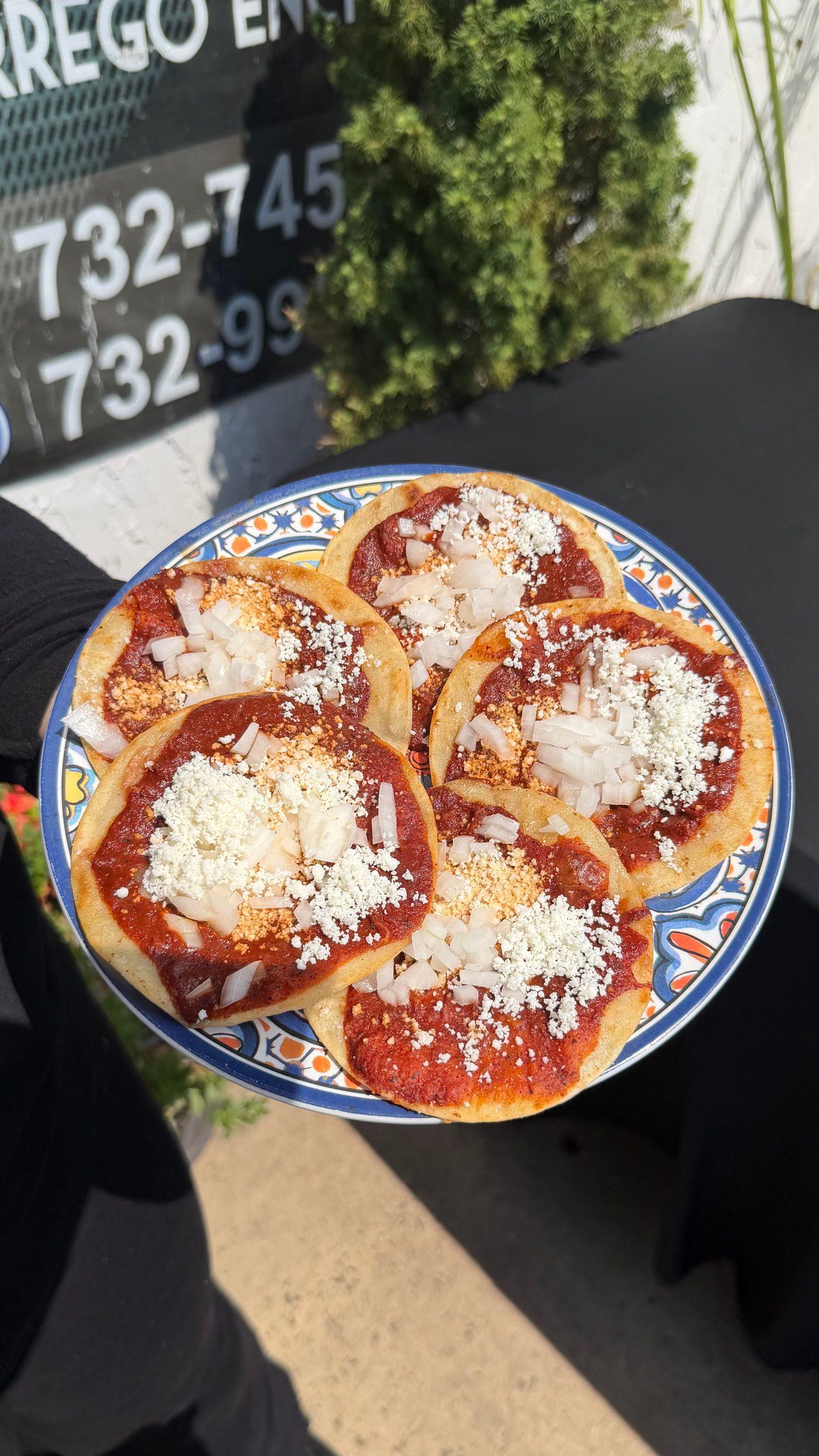 Chalupas poblanas: five small corn tortillas topped with red salsa, chopped onion and queso cotija on a talavera plate