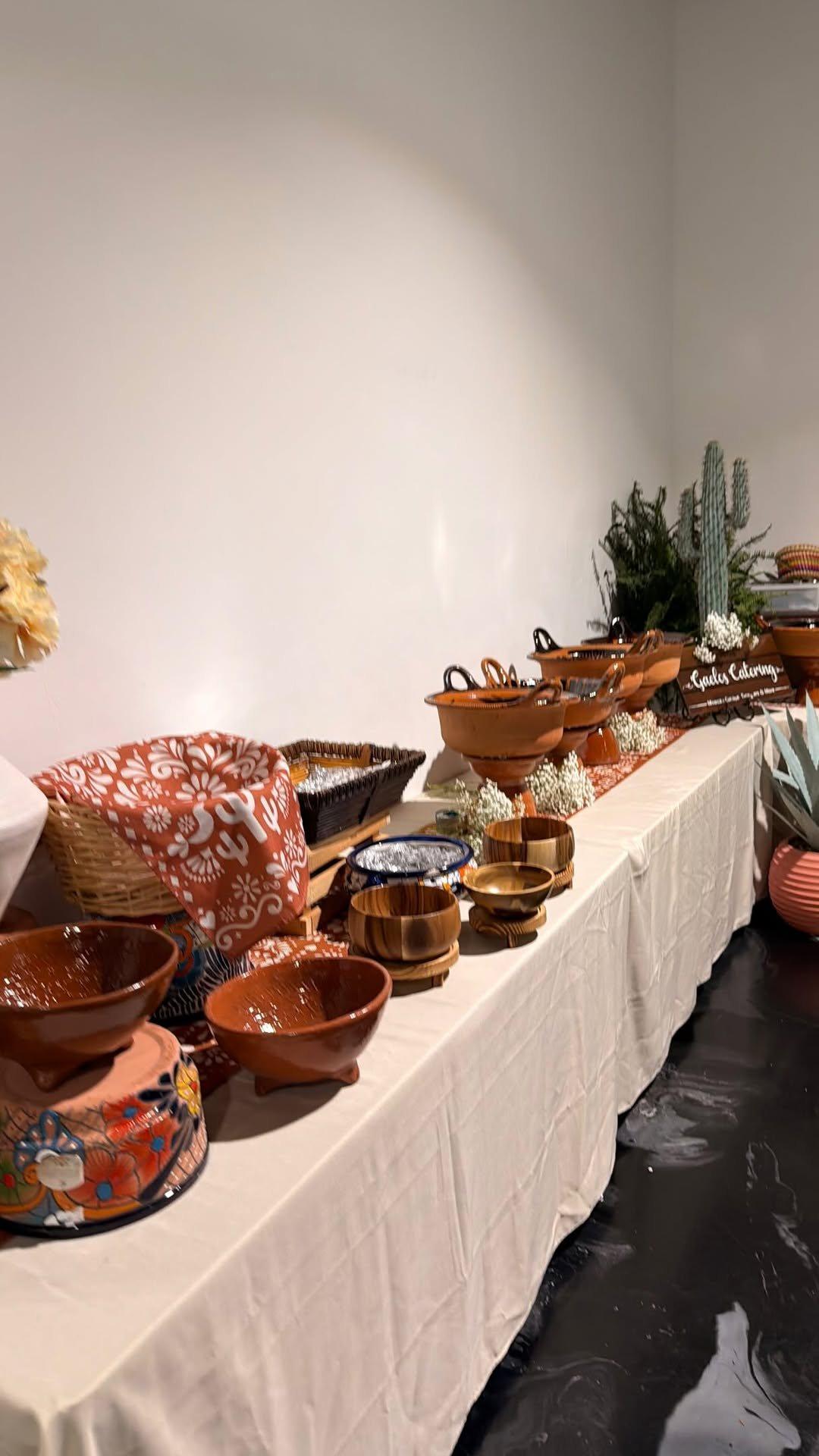 A long Gaelos buffet line of clay pots and serving bowls on white tablecloths at a wedding
